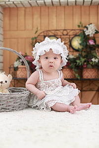 toddler in white dress sitting beside basket