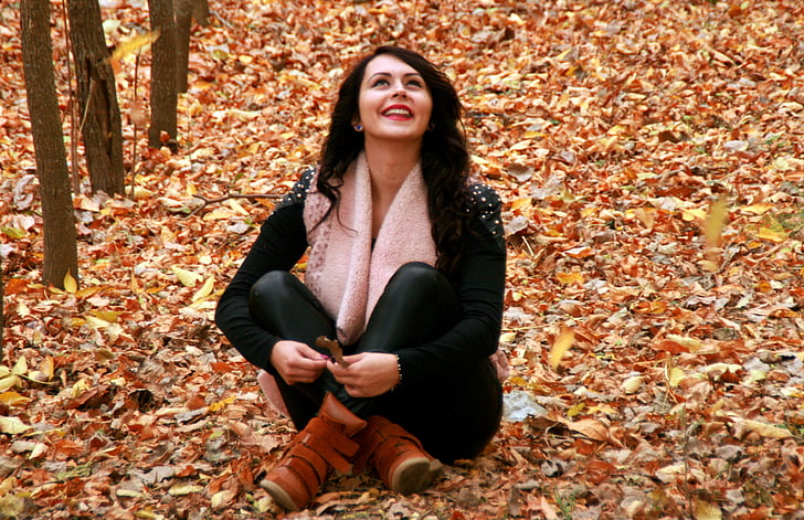 woman in black long-sleeved top and black pants sitting on brown leaves