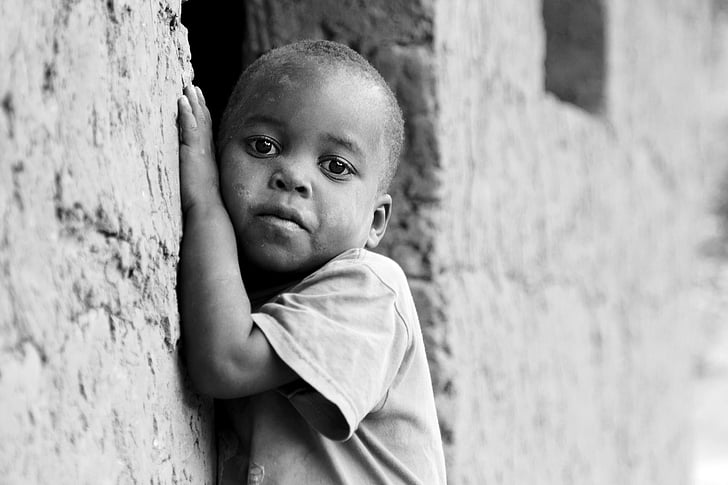 grayscale photo of toddler leaning beside concrete wall