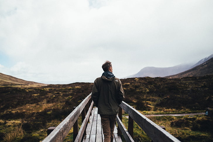 man standing on wooden bridge near mountain range