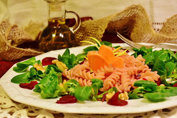 pasta with carrots, vegetable salad and bacon on round white plate