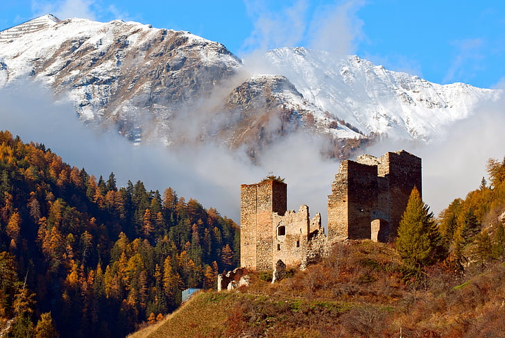beige concrete ruins surrounded with tall trees near snow capped mountain at daytime
