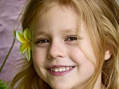 smiling girl with yellow plumeria flower on her ear