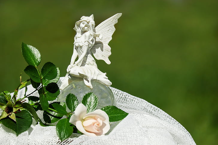 white fairy figurine on white cloth next to white rose