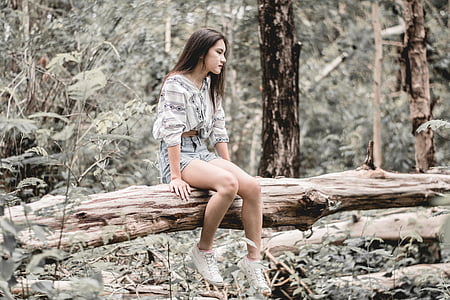 woman sitting on log near trees