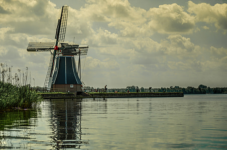 green and black windmill beside body of water under white cloudy sky at daytime