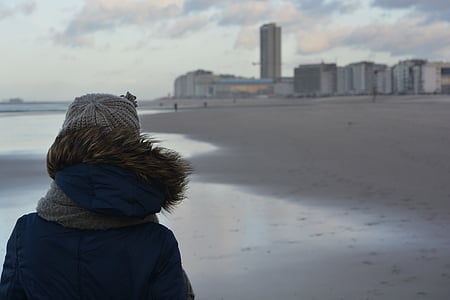 person wearing black and brown hoodie standing on gray beach shore during daytime