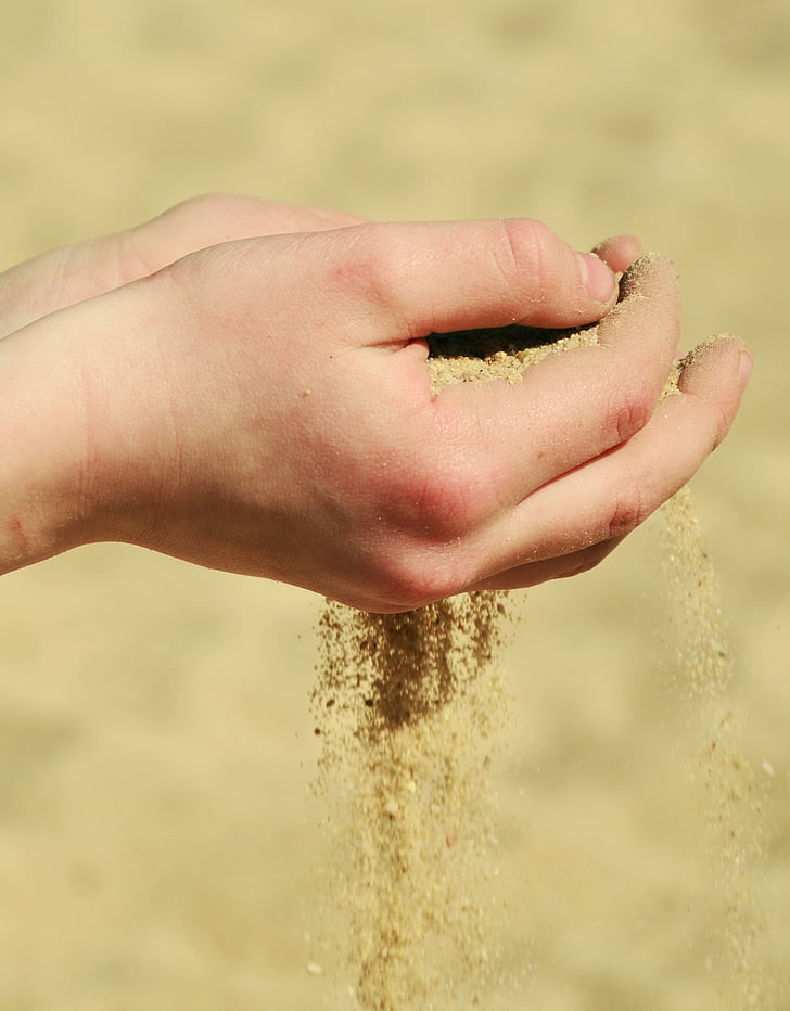 person holding brown sand at daytime
