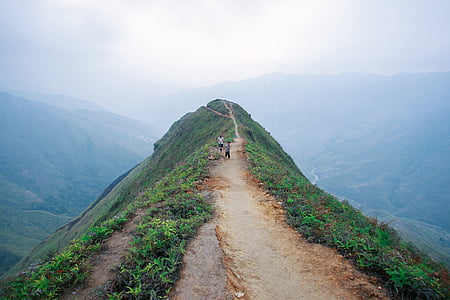 people walking on pathway above hill