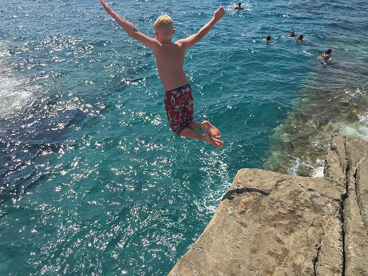 jumping boy on cliff during daytime