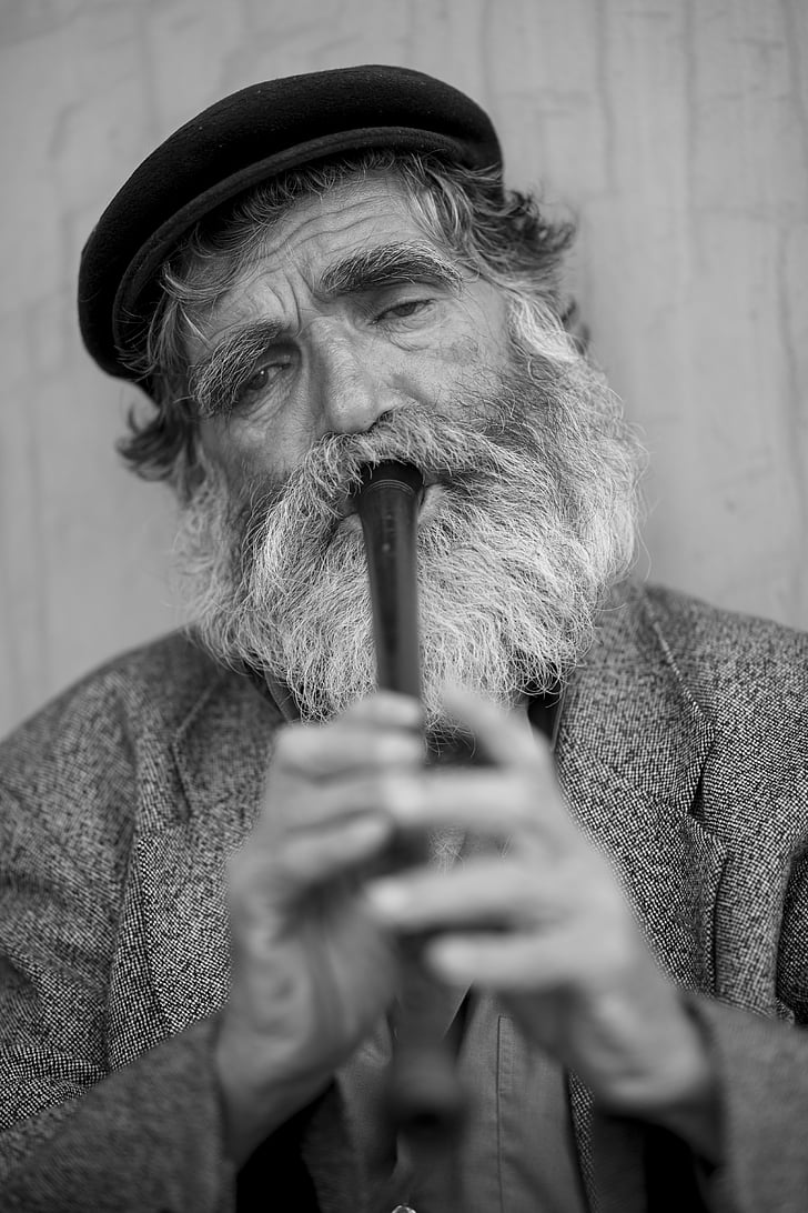greyscale photo of bearded man playing flute