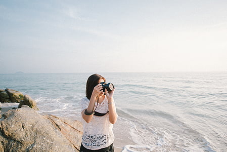 woman holding camera standing beside body of water