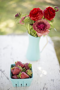 red strawberries in bowl and red flowers in vase