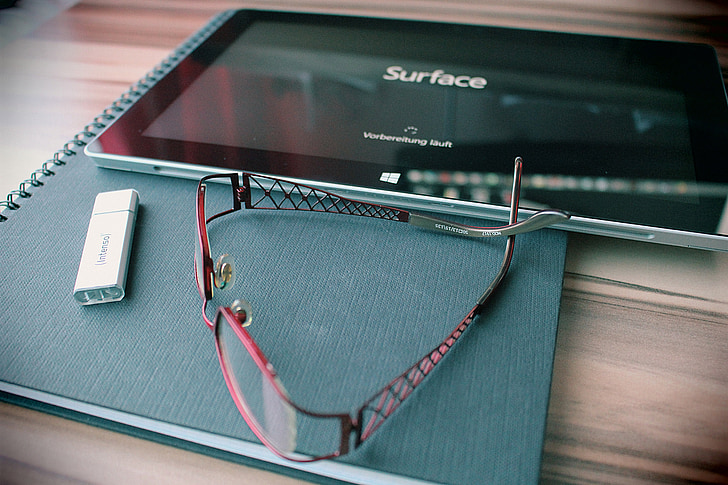 red framed eyeglasses near black Microsoft Surface Pro on top of table