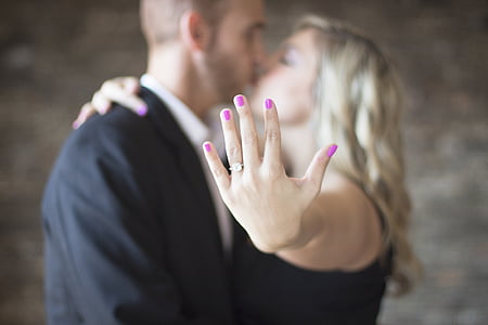 man and woman kissing while woman showing her wedding ring
