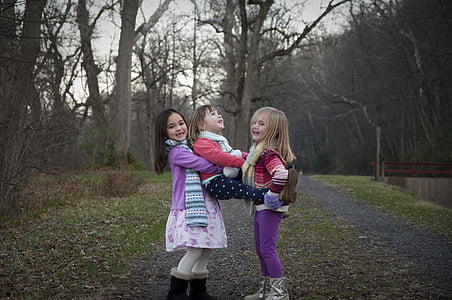 three girls playing near trees during daytime