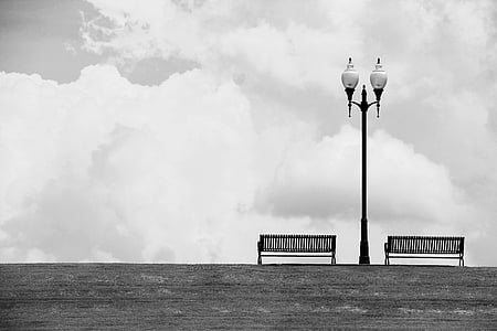 grayscale photo of lamp post near two benches