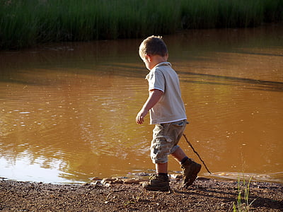 boy wearing gray polo shirt standing beside body of water