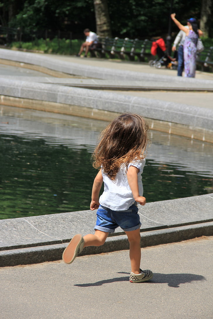 girl wearing white t-shirt runs beside pond at daytime