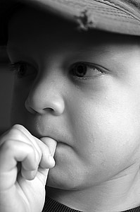 grayscale photography of boy wearing cap with thumb in mouth