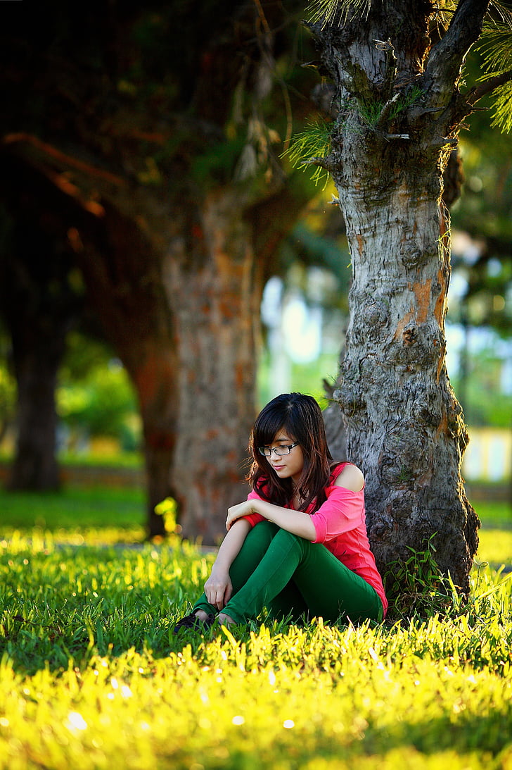 woman in pink cold-shoulder shirt and green leggings sitting under tree