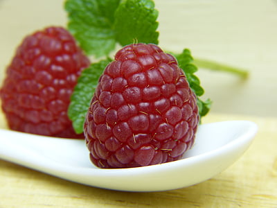 two red raspberries on white ceramic tray