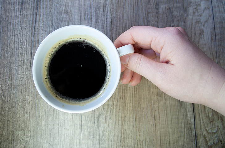 person holding white ceramic mug filled with black coffee