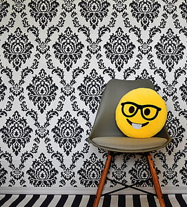 yellow emoji pillow on brown wooden framed gray padded chair