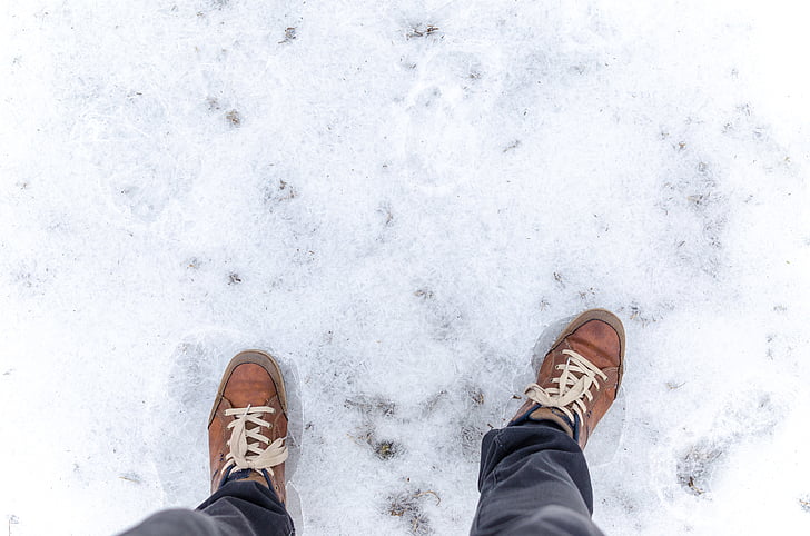 person on brown lace-up shoes standing on snow field