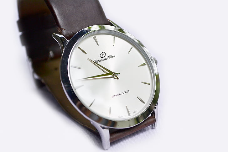 silver-colored analog watch with brown leather strap on top of white surface