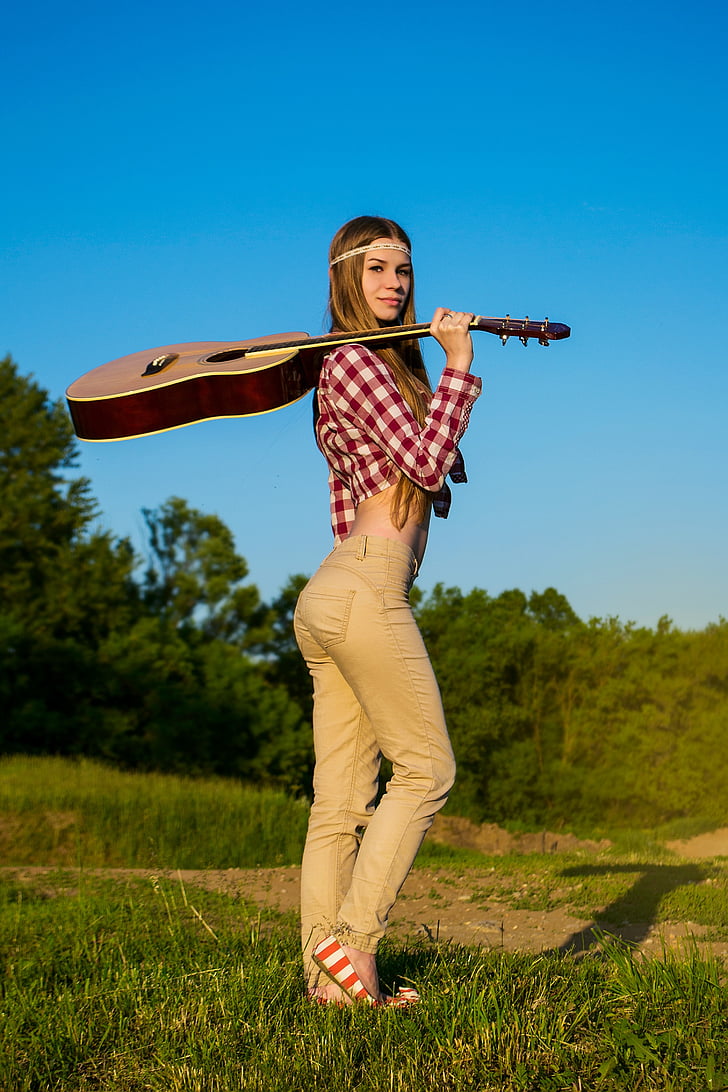 woman carrying brown and white acoustic guitar on green grass during daytime