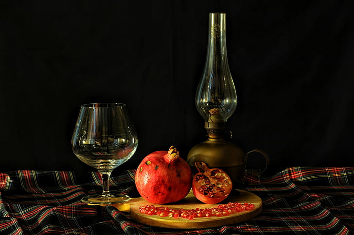 pomegranate between wine glass and oil lamp on table