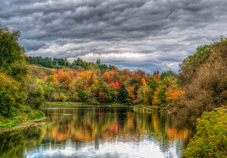lake surrounded by trees under heavy clouds