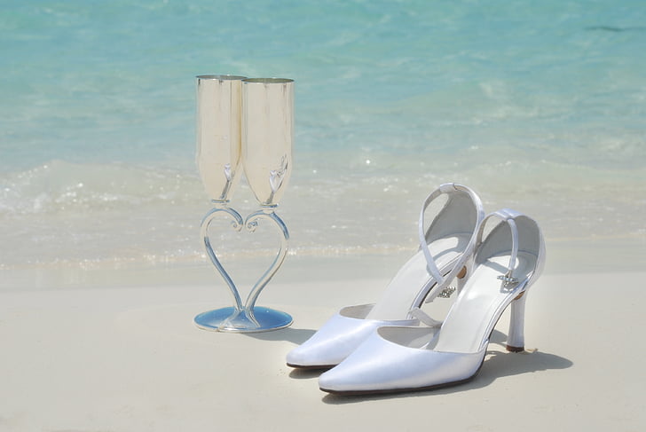 pair of white pointed-toe pumps near wine glasses in seashore