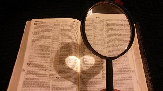person holding black handled magnifying glass near book page