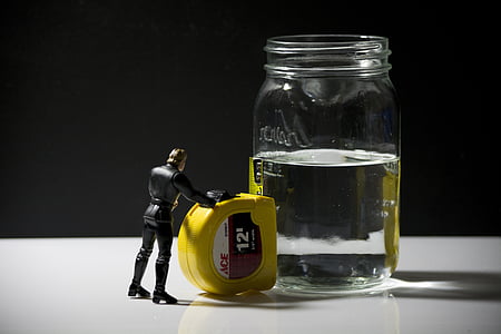 Luke Skywalker action figure placed next to 12-feet yellow ACE steel tape and clear liquid half-filled glass jar