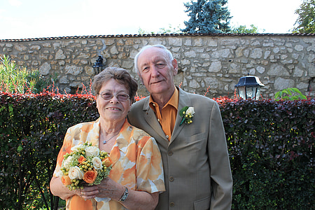 man wearing gray blazer beside woman wearing orange and white floral blazer holding bouquet taking photo at daytime