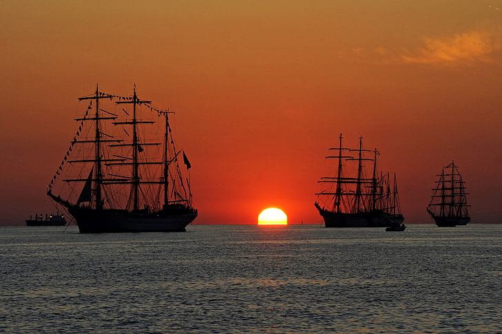 three galleon on body of water during sunset