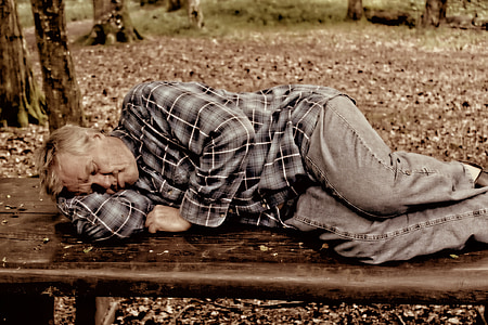man in black pants sleeping on brown bench