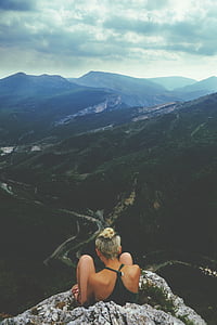 woman wearing black halter top sitting on gray hill in front of mountains