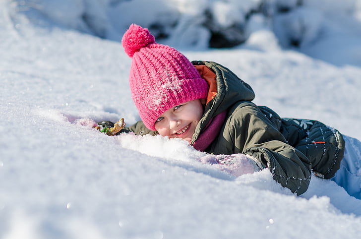 toddler in gray jacket lying on snow field