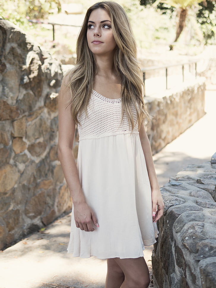 woman in white scoop-neck sleeveless dress standing near wall