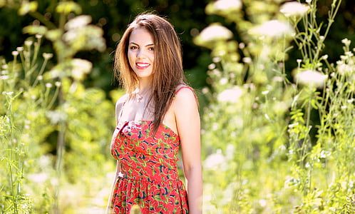 smiling woman wearing multicolored floral spaghetti strap dress standing beside tall plants