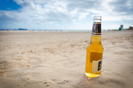 clear glass beer bottle on sand under cloudy sky