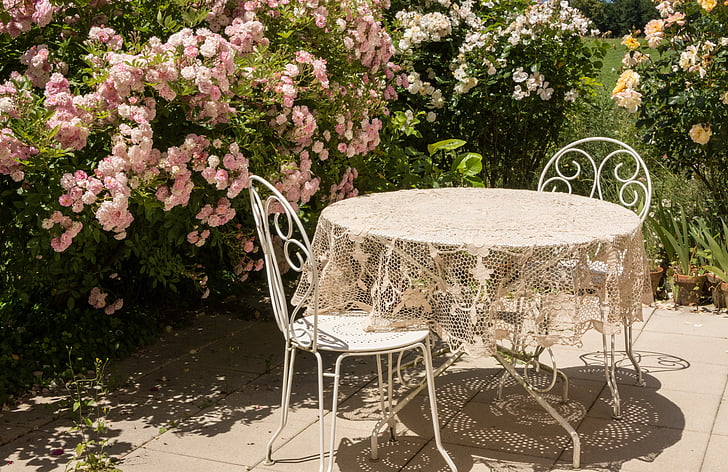 beige floral table cover on round white patio table beside two chairs