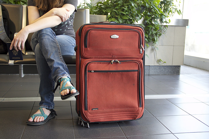 woman sitting beside red travel luggage