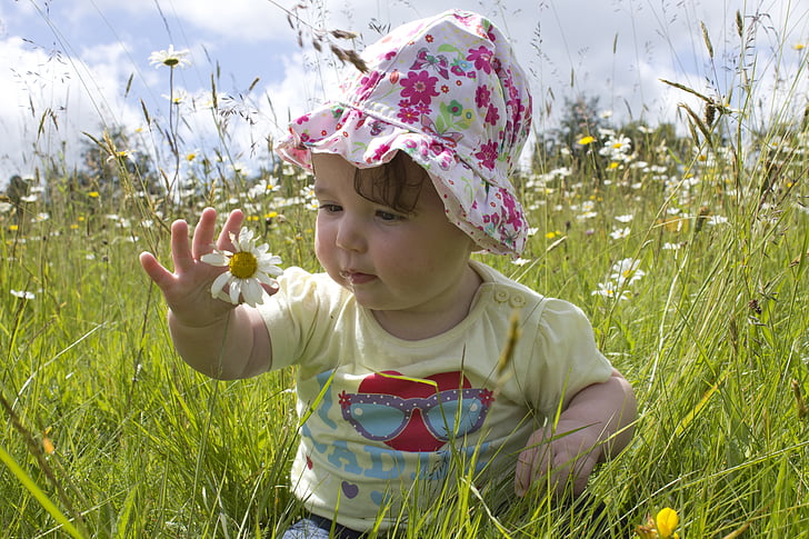 photo of baby sitting on white petaled flower field during daytime
