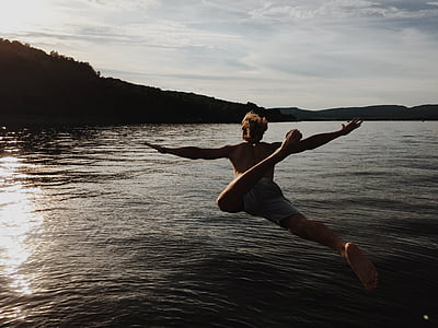 man wearing gray shorts jumping towards body of water during daytime