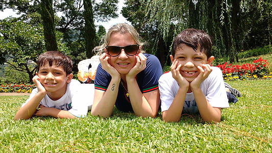 woman lying on grass beside two boys during daytime