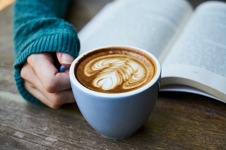 person holding white ceramic mug with coffee latte